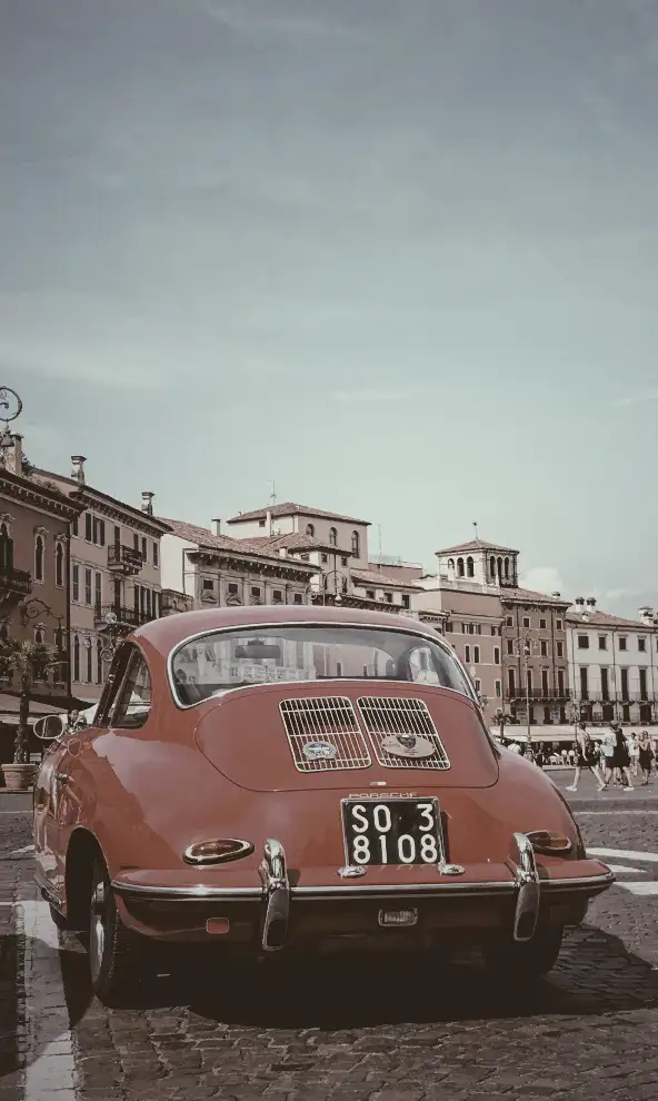 Red car against old buildings in Verona city, Italy, with CSS saturate filter set to 20%, resulting in a more grayish appearance compared to the original photo.