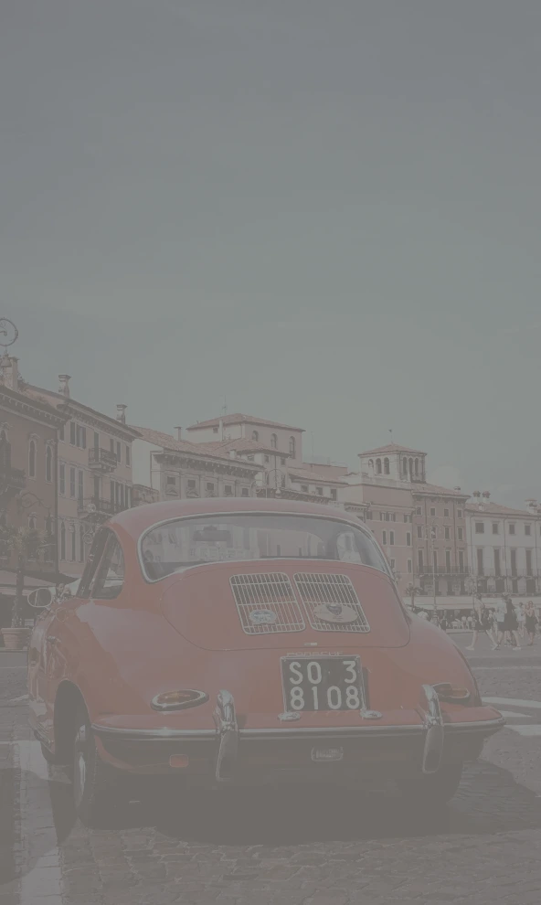 A photo of a red car with old buildings in the background, captured in Verona, Italy. The image has a CSS filter with 20% contrast, giving it a softer, more grayish look compared to the original.