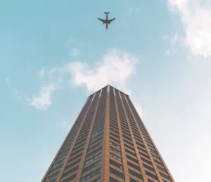 This image displays a photo of a brown building with the sky in the background and an airplane flying overhead.