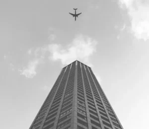 This image displays a photo of a brown building and the sky with an airplane. The CSS grayscale filter is set to 100%, converting the entire photo into grayscale shades.