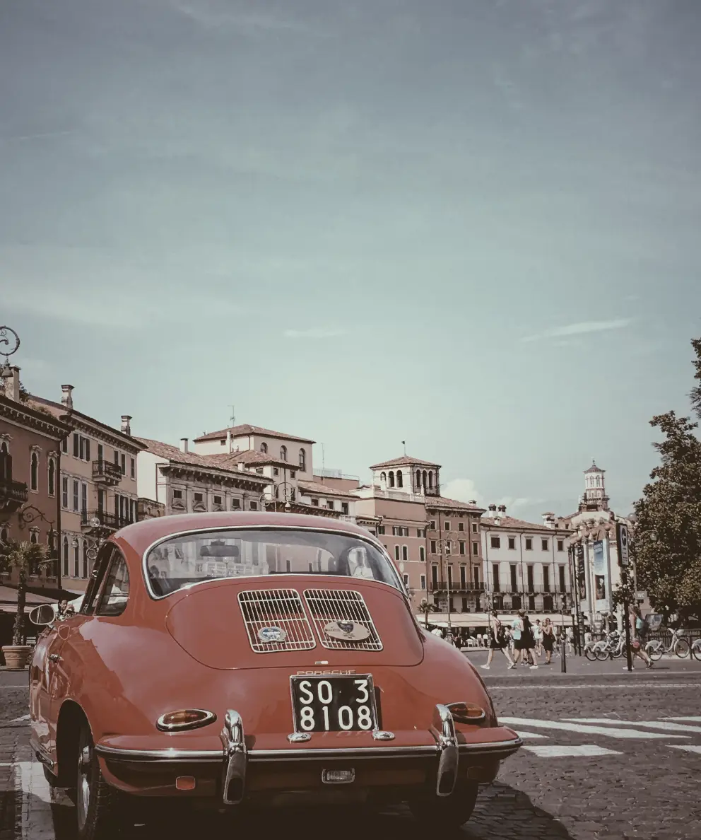 Utilizing the grayscale filter. This image shows a photo of a red car with old buildings as a background.This photo was captured in Verona city Italy. We set the css filter: grayscale(50%).